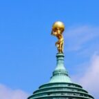 Golden statue of Atlas struggling under weight at the top of a copper building roof.