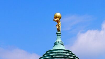 Golden statue of Atlas struggling under weight at the top of a copper building roof.