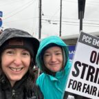 Two wet women in raincoats on a rainy day. One is holding a sign that says PCC Employees on strike for fair pay.