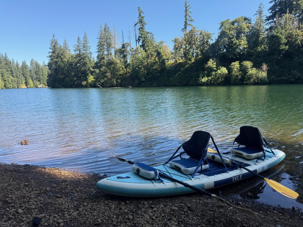 Kayak and two paddles next to a lake with green trees in a background and a blue sky